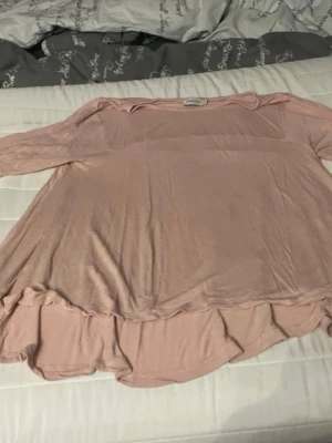 Ljusrosa volangtopp med lång ärm - Söt ljusrosa topp med volangkant nertill och lång ärm. Modellen är lös och flowy, perfekt för en avslappnad stil. Tunt och mjukt material som känns skönt mot huden.