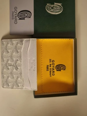 Vit kortplånbok från Go4yard - Snygg och exklusiv vit kortplånbok från Go4yard med klassiskt mönster och flera kortfack. Tillverkad i läder och canvas, levereras med originalask och tygpåse. Perfekt för dig som vill ha en stilren accessoar med lyxig känsla.