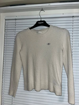 Vit stickad tröja från Gant - Klassisk vit stickad tröja från Gant med rund halsringning och diskret broderad logga på bröstet. Tröjan har långa ärmar och ribbstickade muddar vid ärmslut och nederkant. Den är bomulls material, helt oanvänd typ som ny. Väldigt varm och skön.