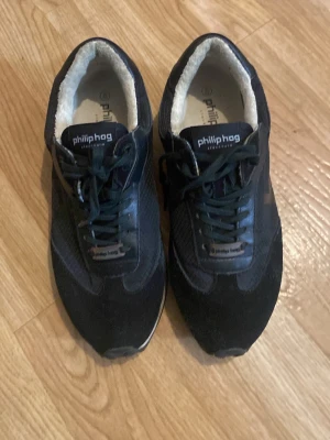 Svarta sneakers från Philip Hog - Snygga svarta sneakers från Philip Hog med ovandel i mocka och mesh. Skorna har vita innersulor och klassisk snörning. Yttersulan är vit och svart vilket ger en sportig look. Perfekta för dig som gillar stilrena och bekväma sneakers. Priset kan diskuteras vid snabb affär.