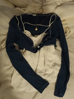 Blå bolerotopp - Säljer en snygg kombo med en marinblå bolerotopp med långa ärmar. Koftan är kroppan som är perfekt för lager-på-lager-stil och passar till jeans eller kjol. ENDAST den blåa koftan, den vita toppen kommer inte med. Vita tröjan är endast där för att visa hur man kan lagra koftan.