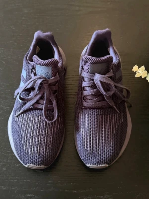 Lila Adidas sneakers i mesh - Säljer ett par lila Adidas sneakers med klassiska ränder på sidorna. Skorna har ovandel i ventilerande meshmaterial och snörning framtill. Sulan är vit och ger en sportig look. Perfekta för dig som gillar stilrena och bekväma skor.