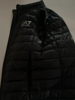 Svart dunväst från EA7 Emporio Armani, Pris kan diskuteras  - Snygg svart dunväst från EA7 Emporio Armani. Perfekt för sommaren och har en stilig look