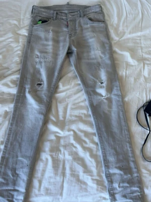 Ljusgrå slitna dsquared2 jeans - Säljer ett par ljusgrå jeans med slitningar på benen. Jeansen har klassisk femficksmodell. Perfekta för en avslappnad och trendig look. Storlek: 44*