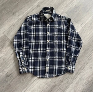 Abercrombie and fitch skjorta - Snygg blårutig skjorta från Abercrombie & Fitch med klassisk krage och vita knappar. Skjortan har en bröstficka och är långärmad. Perfekt för dig som gillar en avslappnad men stilren look. Storlek M men passar liten på mej som vanligtvis har M så närmre S. 