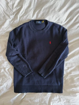 Mörkblå stickad tröja från Polo Ralph Lauren - Mörkblå stickad tröja från Ralph Lauren med klassisk rund halsringning. Tröjan är i mycket gott skick med minimala tecken på användning. Hör gärna av dig vid frågor eller för fler bilder.