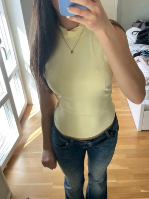 Ljusgul ärmlös topp med hög hals - Snygg ljusgul ärmlös topp med hög hals och tight passform. Perfekt att styla med jeans eller kjol för en sommar look. Mjukt och stretchigt material som sitter bekvämt mot kroppen.
