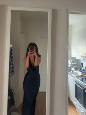 Mörkblå långklänning i satin - Säljer en elegant mörkblå långklänning med smala axelband och v-ringad hals. Klänningen har en figurnära passform och är tillverkad i glansigt satinmaterial som ger en lyxig känsla. Perfekt för dig som vill sticka ut på nästa bal eller fest.