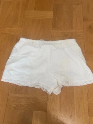 Vita shorts med spets från BikBok - Säljer ett par vita shorts från BikBok i storlek XS. De har elastisk midja med snörning och fina spetsdetaljer längs nederkanten. Perfekta för sommarens varma dagar och har en mjuk och luftig känsla.