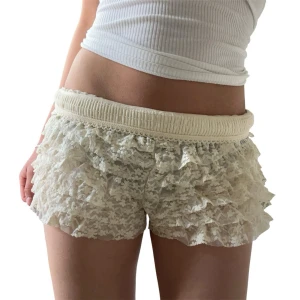 Beige spetsvolang shorts - Säljer ett par beigevita shorts med flera lager volanger i spets. De har elastisk midja och en romantisk look som passar perfekt för sommarens varma dagar. Materialet är mjukt och luftigt, vilket gör dem riktigt bekväma att bära.