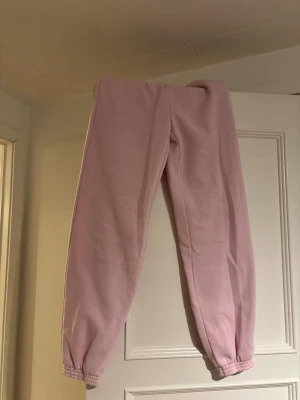 Ljusa rosa mjukisbyxor med resår - Säljer ett par ljusa rosa mjukisbyxor med resår vid benslut. Byxorna har en klassisk relaxed fit och är gjorda i mjukt material som är perfekt för chill dagar. Inga synliga loggor eller fickor, enkel och clean design.