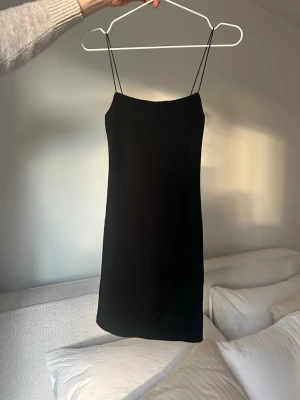 Svart kort klänning från Zara - En stilren svart kort klänning från Zara med tunna axelband och figurnära passform. Perfekt för dig som gillar minimalistisk stil. Klänningen är enkel och tidlös, vilket gör den lätt att matcha med olika accessoarer.