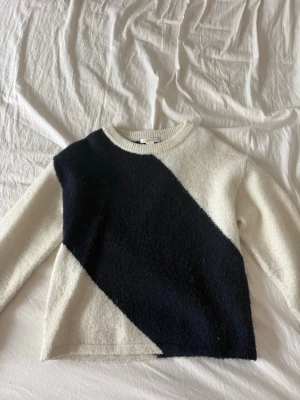 Vit och svart stickad tröja - Snygg stickad tröja i vitt med en bred diagonal svart panel framtill. Tröjan har rund halsringning och långa ärmar. Perfekt för dig som gillar enkel men cool design.
