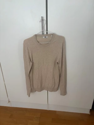 Beige stickad tröja med rund hals - En stilren beige stickad tröja med rund halsringning och långa ärmar. Tröjan har en enkel design utan mönster och ribbstickade muddar vid ärmslut och nederkant. Perfekt att matcha med jeans