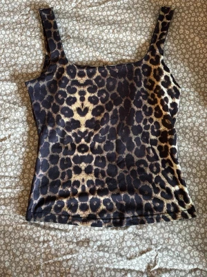 Leopardmönstrad linnetopp - Snygg leopardmönstrad linnetopp med breda axelband och fyrkantig ringning. Toppen är figurnära och har en mjuk, stretchig känsla som passar perfekt till jeans eller kjol. Materialet känns som polyester och färgerna går i brunt, svart och beige. 💘