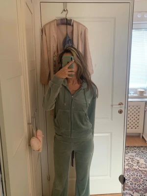 Grön velour loungewear-set Gina Tricot  - Mysigt loungewear-set i mjuk grön velour med zip-tröja och matchande byxor. Tröjan har huva och dragkedja framtill, byxorna har utsvängda ben och resår i midjan. Perfekt för chill dagar hemma. Banden finns inte kvar runt byxorna