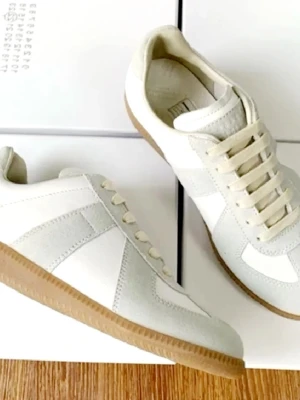 Vita sneakers från Maison Margiela Utan Box - Stilrena vita sneakers från Axel Arigato med beige detaljer och klassisk gummisula. Skorna har ovandel i läder och mocka, vita snören och låg profil. Perfekta för en clean och modern look.