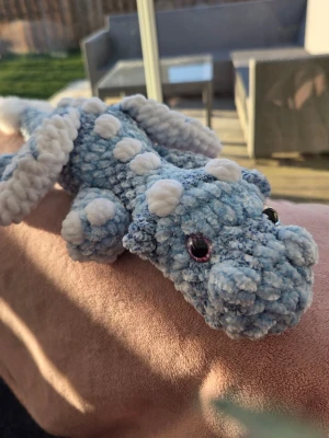 Blå virkad drake med vita detaljer - Supermjuk och fluffig virkad drake i ljusblått melerat sammetsgarn med vita prickar och vingar. Draken har säkerhetsögon och är handgjord och passar perfekt som prydnad eller gosedjur.