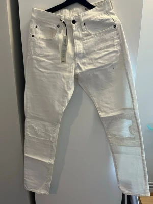 Vita jeans med patchdetaljer - Snygga vita jeans från G-Star RAW med patchade detaljer på benen och klassisk femficksdesign. Jeansen har raka ben och coola sömmar som ger en unik look. Materialet är kraftig denim i bomull och passformen är modern och avslappnad. 30/34 