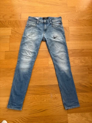 Ljusblå slim fit jeans från Replay - Snygga ljusblå slim fit jeans från Replay med slitningar och lätt tvättad look. Klassisk femficksmodell med läderpatch bak i midjan och dragkedjegylf. Perfekta för en avslappnad och trendig stil.