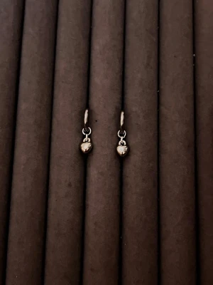 Små silverfärgade örhängen med pärldroppe - Säljer ett par stilrena örhängen i silverfärg med små, blanka pärldroppar som hänger från tunna ringar. Perfekta för dig som gillar minimalistisk och elegant stil. Materialet ser ut att vara metall med en polerad finish.