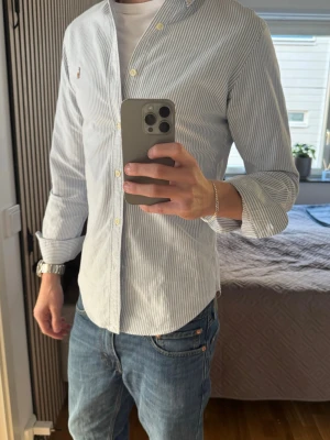 Randig skjorta från Ralph Lauren - Klassisk vit skjorta med tunna blå ränder från Ralph Lauren. Skjortan har button-down krage, långa ärmar och små knappar framtill. Liten broderad logga på bröstet. Skicket är i topp och inga defekter, skjorta använts länge och det visar bara på bra kvalitet, pris går alltid att diskuteras