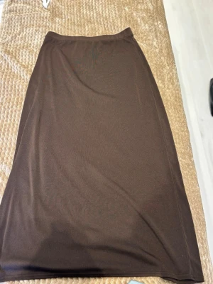 Brun lång kjol i mjukt tyg - En enkel och stilren brun lång kjol med rak passform. Kjolen är gjord i ett mjukt och stretchigt material som känns bekvämt mot huden. Perfekt för dig som gillar minimalistisk och klassisk stil.