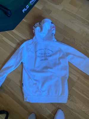 Vit hoodie rich - Säljer en vit hoodie från Hoodrich i storlek XS. Hoodien har tryck på ryggen och coola detaljer på huvan med svarta och röda linjer. Tillverkad i mjukt bomullsmaterial och har en klassisk huva. Perfekt för dig som gillar streetwear och vill sticka ut. Har använts 1-2 gånger 