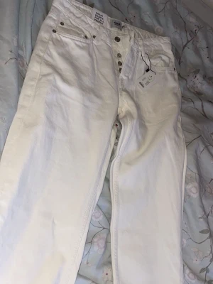Vita jeans från 157 med knappar - Snygga vita jeans från 157 med klassisk femficksdesign och silverfärgade knappar framtill. Jeansen har raka ben och är gjorda i ett mjukt bomullsmaterial. Perfekta för dig som vill ha en clean och fräsch look. Ord pris 150kr 