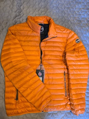 Orange dunjacka från Colmar - Snygg orange dunjacka från Colmar med quiltad design. Jackan har två dragkedjeförsedda fickor och logotyp på ärmen. Perfekt lättviktsjacka för svala dagar och tillverkad i lätt, isolerande material.