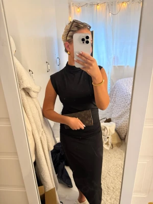 Svart ärmlös långklänning - Stilren svart långklänning med hög hals och ärmlös design. Klänningen har en smickrande passform och är perfekt för dig som gillar minimalistisk och elegant stil. Tillverkad i ett mjukt och följsamt material som ger en snygg siluett.