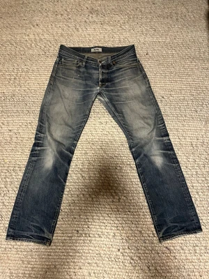 Archive Acne Jeans - Säljer ett par blå jeans från Acne med snygga slitningar och tvättade detaljer. Klassisk femficksmodell med raka ben och normal midja. Jeansen är tillverkade i denim och har en cool, lite blekt look som passar perfekt till en avslappnad stil.