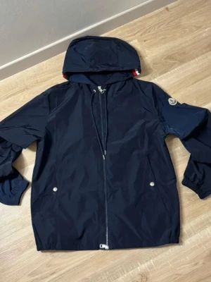 Mörkblå vindjacka med huva - Säljer en mycket vindjacka i absolut nyskick. Storleken är en Moncler 1, vilket passar dig som bär Small eller en mindre Medium. Jackan är felfri och sparsamt använd. Priset är 1 899 kr, men jag kan tänka mig att diskutera priset vid en snabb och enkel affär. Skicka ett meddelande vid intresse eller om du vill ha fler bilder!