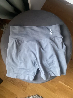 Grå  träningsshorts DFYNE - Säljer ett par grå  träningsshorts från DFYNE med bred ribbad midja och logotyp framtill. Materialet är stretchigt och passar perfekt för gym eller löpning. Shortsen har en kroppsnära passform och är tillverkade i ett mjukt syntetmaterial.