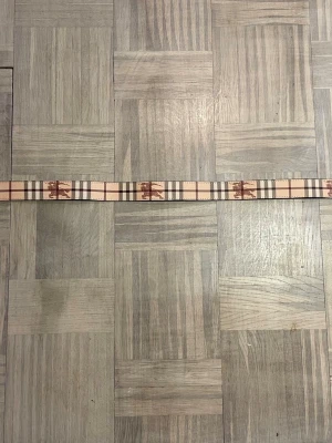 Beige rutigt Burberry bälte - Säljer ett beige bälte från Burberry med klassiskt rutigt mönster och en stor metallspänne med TB-logga. Bältet har bruna och svarta detaljer och är tillverkat i skinn. Perfekt för att lyfta din outfit.
