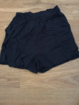 Svarta shorts från PIECES - Säljer ett par svarta shorts från PIECES i storlek XS. De har en enkel design med elastisk midja och är tillverkade i ett lätt tyg som passar perfekt till varmare dagar.