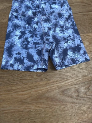 Gråmönstrade cykelshorts från Stronger - Säljer ett par grå och svarta cykelshorts från Stronger med coolt batikmönster. Shortsen har en tight passform och är tillverkade i stretchigt funktionsmaterial. Logga i silver på ena benet. Perfekta för träning eller chill.