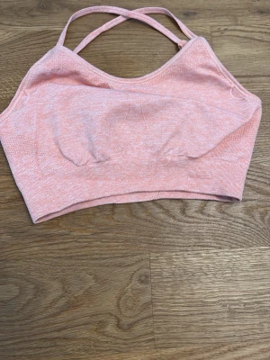 Rosa sport-bh med korsade band - Säljer en ljusrosa sport-bh med korsade axelband och sömlös design. Bh:n är tillverkad i ett stretchigt material som ger bra komfort och stöd. Passar perfekt för träning eller avslappnade dagar. Märket är Aim'n, vilket syns på baksidan.
