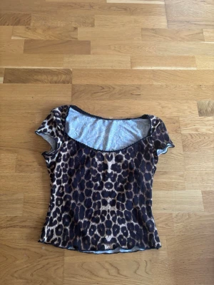 Leopardmönstrad topp med kort ärm - Cool topp med leopardmönster i mörka och beige toner. Modellen är figurnära med korta ärmar och rundad halsringning. Perfekt för dig som vill sticka ut och addera lite edge till din outfit.