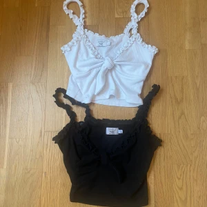 Två ribbade toppar med volangkant och knyt från NA-KD x Pamela - Två ribbade linne-toppar från NA-KD x Pamela, en svart och en vit. Båda har volangkant längs axelband och urringning samt knyt framtill. Perfekta för sommaren och lätta att matcha.