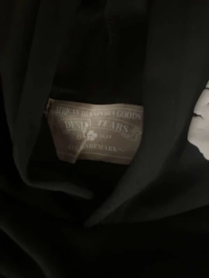 Svart hoodie - Svart hoodie med vita grafiska blommönster över hela plagget. Hoodien har huva och ribbade muddar vid ärmslut och nederkant. Materialet är mjukt och bekvämt, perfekt för dig som gillar streetwear och unik design.
