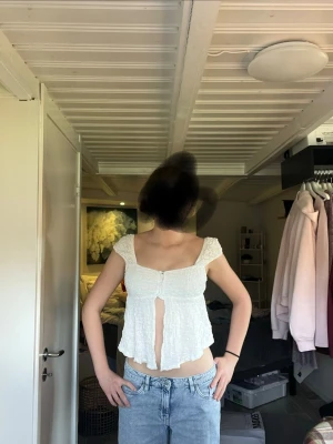 Vit croppad topp  - Säljer en vit croppad topp. Toppen har en lätt volang och öppen front, perfekt för dig som gillar en luftig och trendig stil. Materialet är bomull och toppen har en feminin v-ringning.
