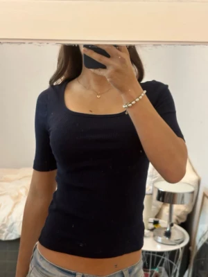 Marinblå ribbad topp från Kappahl - Säljer en marinblå ribbad topp från Kappahl i storlek XS. Toppen har en snygg fyrkantig halsringning och korta ärmar. Perfekt att matcha med jeans eller kjol för en cool och enkel look.