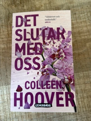 Det slutar med oss av Colleen Hoover - Säljer boken 'Det slutar med oss' av Colleen Hoover. Omslaget är ljusrosa med stora lila bokstäver och en krossad blomma. Pocketformat, tryckt på papper. Perfekt för dig som gillar gripande och romantisk skönlitteratur.