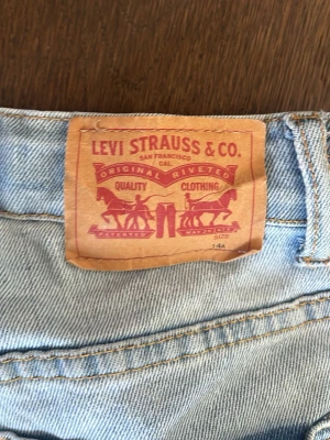 Ljusblå Levi's jeans med klassisk passform - Säljer ett par ljusblå Levi's jeans med klassisk femficksmodell och ikonisk läderpatch bak. Jeansen har raka ben och tydliga sömmar i kontrastfärg. Perfekta för en avslappnad och tidlös stil.