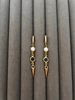 Guldörhängen med pärlor och svarta detaljer - Snygga hängande örhängen i guldton med vita pärlor, svarta runda detaljer och spetsiga konformade hängen. Örhängena har en modern design och stängs med klicklås. Perfekta för dig som vill ha något unikt och trendigt i smyckeskrinet.