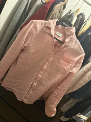 Ljusrosa linneskjorta från Tenison - Snygg ljusrosa skjorta från Tenison i luftigt linne. Skjortan har klassisk krage, knäppning framtill och en bröstficka. Perfekt för en avslappnad men stilren look. Långärmad och med normal passform.