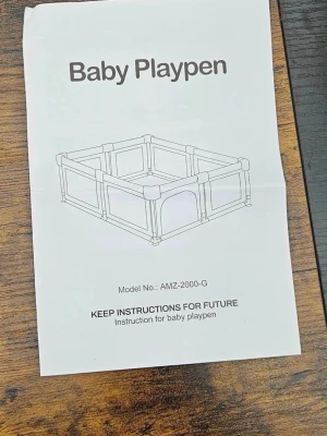 Grå babyhage med färgglada ringar - Säljer en babyhage modell AMZ-2000-G i grått tyg med nätpaneler och metallstänger. Medföljer färgglada plastleksaksringar i grönt, blått, rött och gult. Perfekt för att skapa en säker lekyta för små barn inomhus.