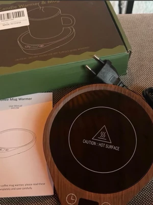 Elektrisk koppvärmare i trälook - Elektrisk koppvärmare med snygg trälook och svart värmeyta. Perfekt för att hålla kaffe eller te varmt vid skrivbordet. Rund form, tydlig varning för het yta och enkel touchkontroll. Levereras med sladd och användarmanual.
