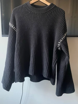 Svart stickad tröja med vita detaljer - Svart stickad tröja med lös passform och vita dekorativa sömmar längs ärmar och axlar. Tröjan har rund halsringning och vida ärmar, perfekt för en avslappnad och trendig look. Supersnygg och PERFEKT passform. Använt varsamt❣️
